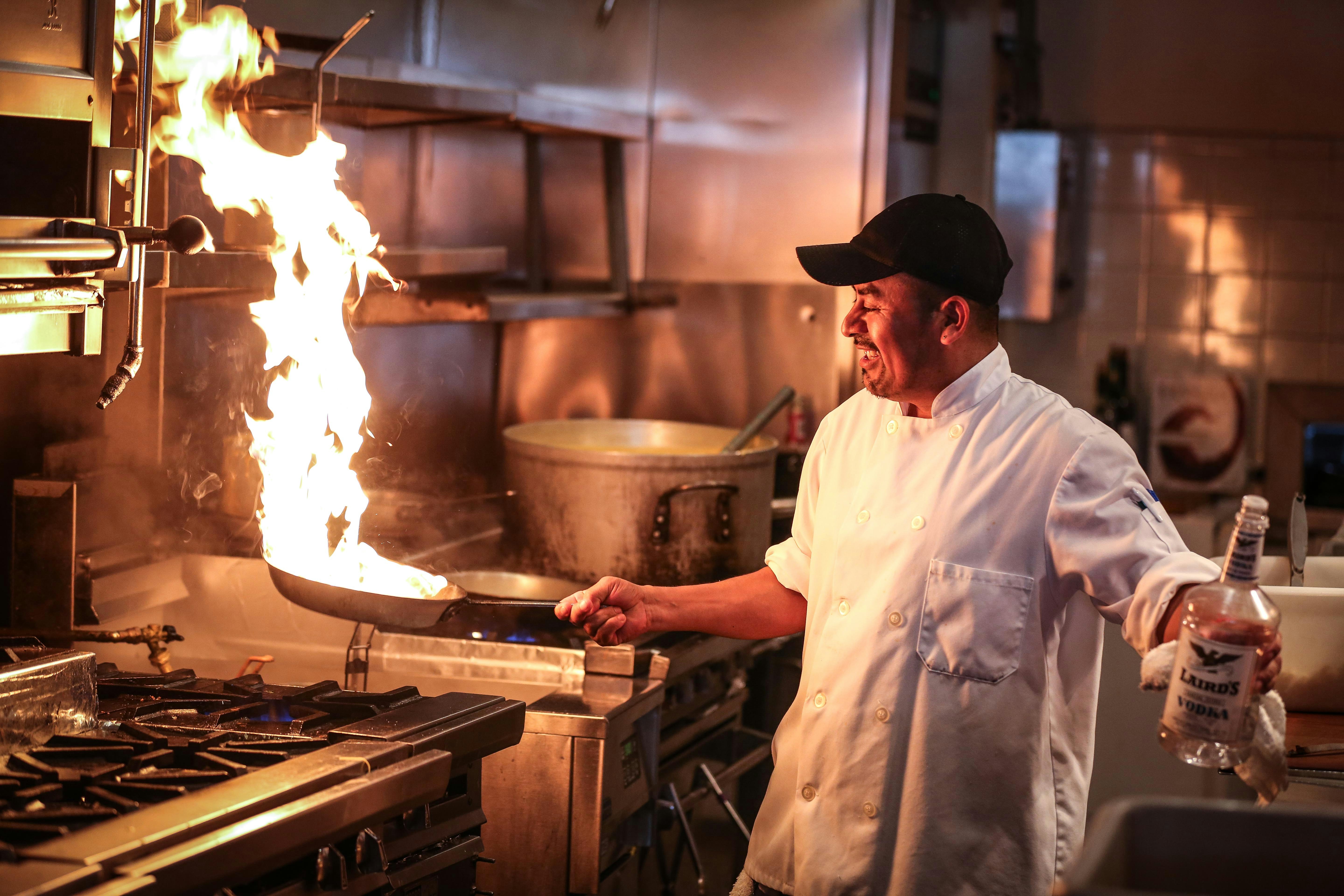Cook in kitchen with a pan on fire in hand